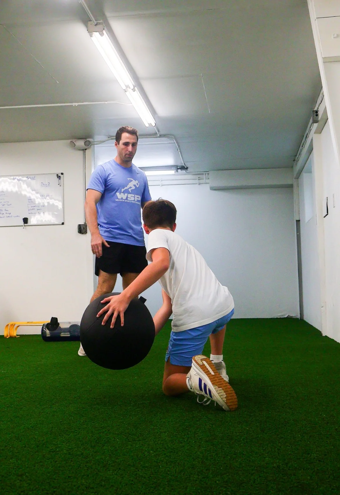 Coach guiding an athlete through a kneeling medicine-ball exercise at WSP