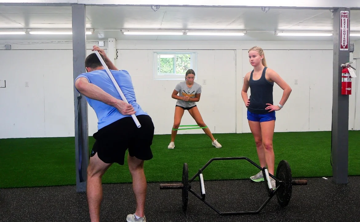 Coach demonstrating hip-hinge technique beside a trap bar at WSP